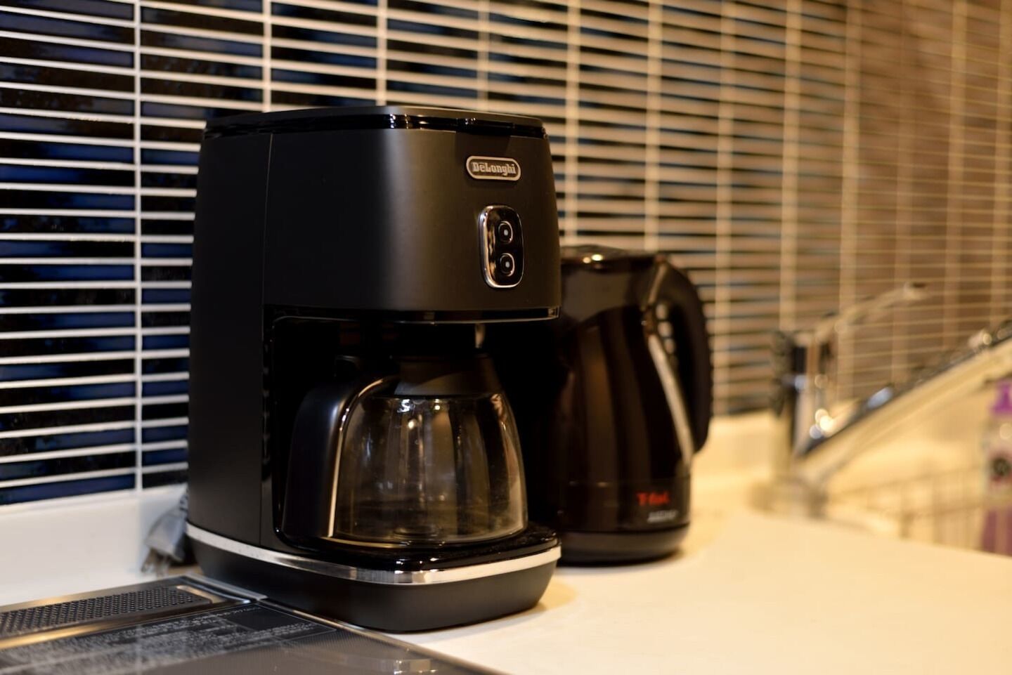 A black coffee maker on a kitchen counter with a window in the background.