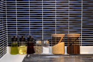 A kitchen counter with various condiments and spices, including bottles of oil, vinegar, and salt, as well as jars of pepper and sugar.