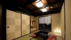 A traditional Japanese room with tatami flooring, a low table, cushions, sliding doors, and a window with a view of the outside. - Machiya Kamo 7 (Kyoto)