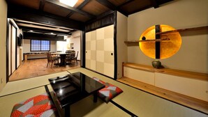 A traditional Japanese room with tatami flooring, a low table, and a sliding door leading to a dining area with a wooden table and chairs. - Machiya Kamo 7 (Kyoto)