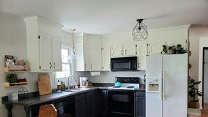 Une cuisine avec des armoires blanches, une cuisinière noire, un four à micro-ondes et un réfrigérateur blanc.