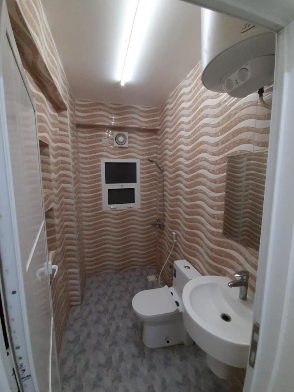 A bathroom with a patterned wall, a toilet, a sink, and a shower.