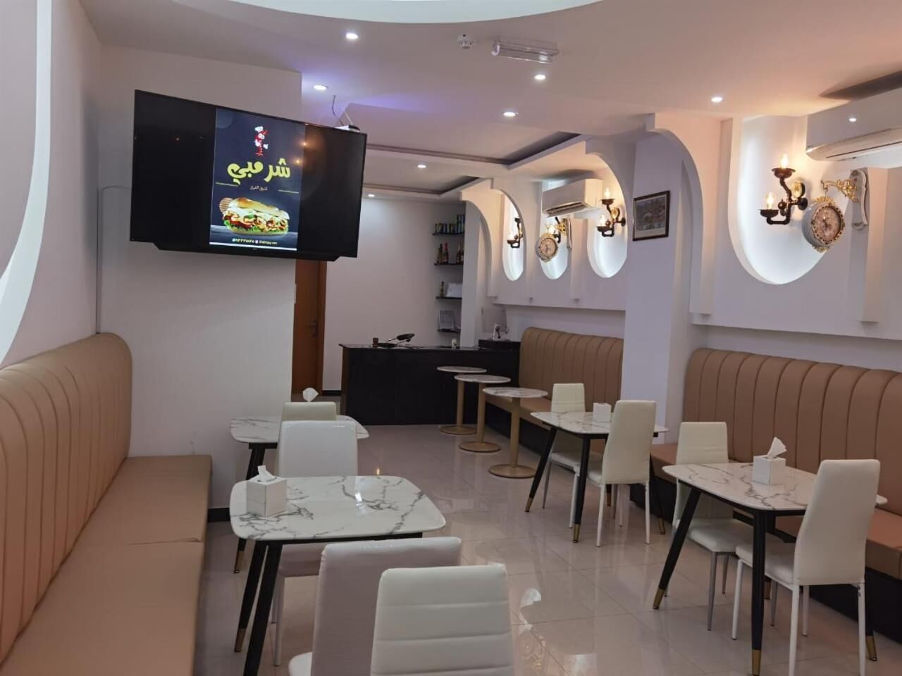 Interior modern d'un restaurant amb disposició de seients, una pantalla de televisió i aplics decoratius a la paret.