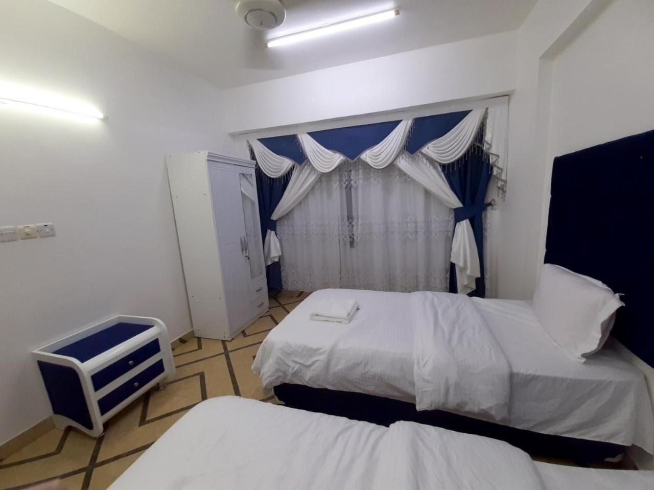 A room with two beds, a wardrobe, a small table, and a window with curtains.