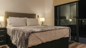 Een moderne hotelkamer met een groot bed, nachtlampen, een donker hoofdeinde en een glazen schuifdeur naar een balkon.