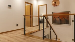 Een modern interieur met een houten trap, glazen balustrade en een hanglamp.