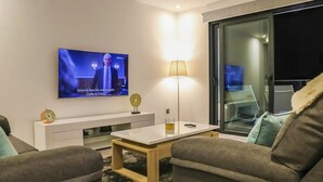 Een moderne woonkamer met een flatscreen televisie, een witte salontafel, een bijzettafeltje en twee banken.