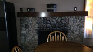 A dining area with a stone fireplace, wooden chairs, and a table. - Lakefront home on Little Barbee that sleeps 6 (Warsaw)