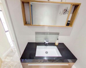A bathroom with a black countertop, a white sink, a mirror above the sink, and a soap dispenser on the countertop. - The Lodge Westmoor Farm (Market Rasen)