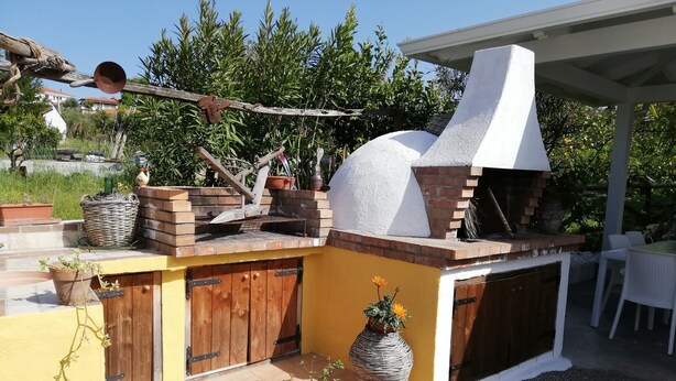 An outdoor kitchen with a brick oven, wooden doors, and potted plants. - Between Tropea and Pizzo: "La Gramigna Villette" in Calabria, 600 meters from the sea (Briatico)