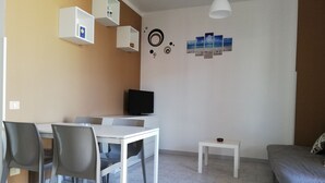 A modern living room with a white table, grey chairs, a flat-screen TV, a small white side table, and a grey sofa. - Between Tropea and Pizzo: "La Gramigna Villette" in Calabria, 600 meters from the sea (Briatico)