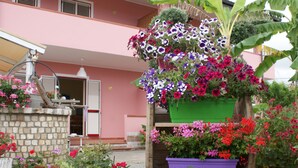 A building with a pink facade, a stone wall, and various flower planters with colorful flowers. - Between Tropea and Pizzo: "La Gramigna Villette" in Calabria, 600 meters from the sea (Briatico)