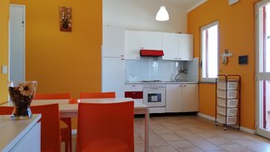 A compact kitchen with white cabinets, a red hood, and a stove. There is a dining area with orange chairs and a table. - Between Tropea and Pizzo: "La Gramigna Villette" in Calabria, 600 meters from the sea (Briatico)
