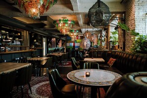 A cozy restaurant interior with wooden tables, leather seating, hanging lights, and a brick wall. - Bryggen Guldsmeden  (Copenhagen)
