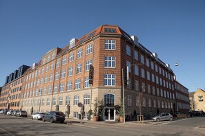 Un grand hôtel à plusieurs étages, avec une entrée d’angle bien visible, de nombreuses fenêtres et une façade en briques.