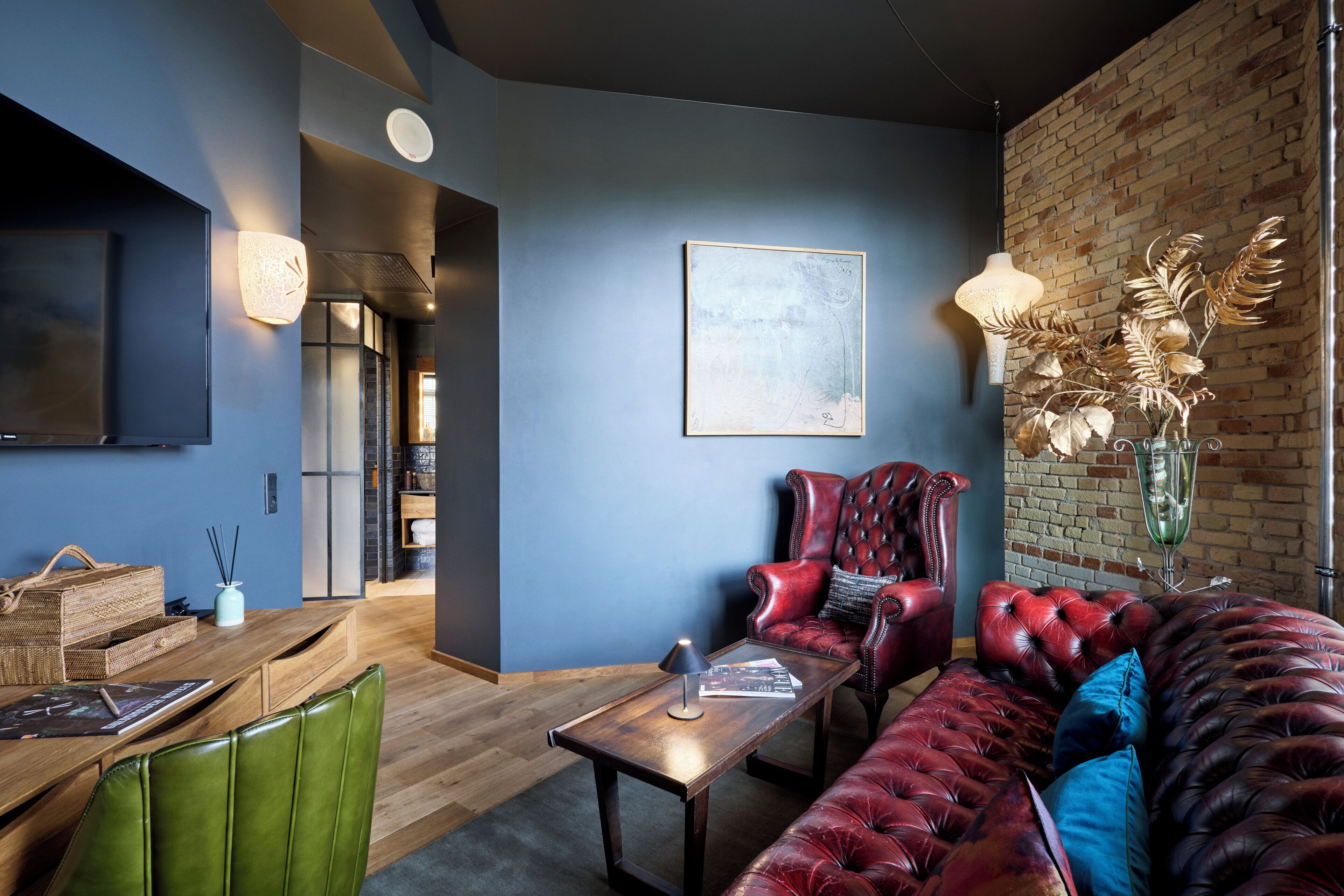 A modern living room with a flat-screen TV, a wooden coffee table, a red leather sofa, and a brick wall.