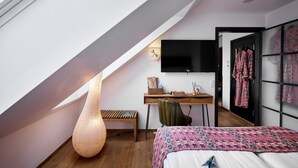 A modern bedroom with a sloped ceiling, a large bed, a desk, a chair, a wall-mounted TV, and a wardrobe. - Bryggen Guldsmeden  (Copenhagen)