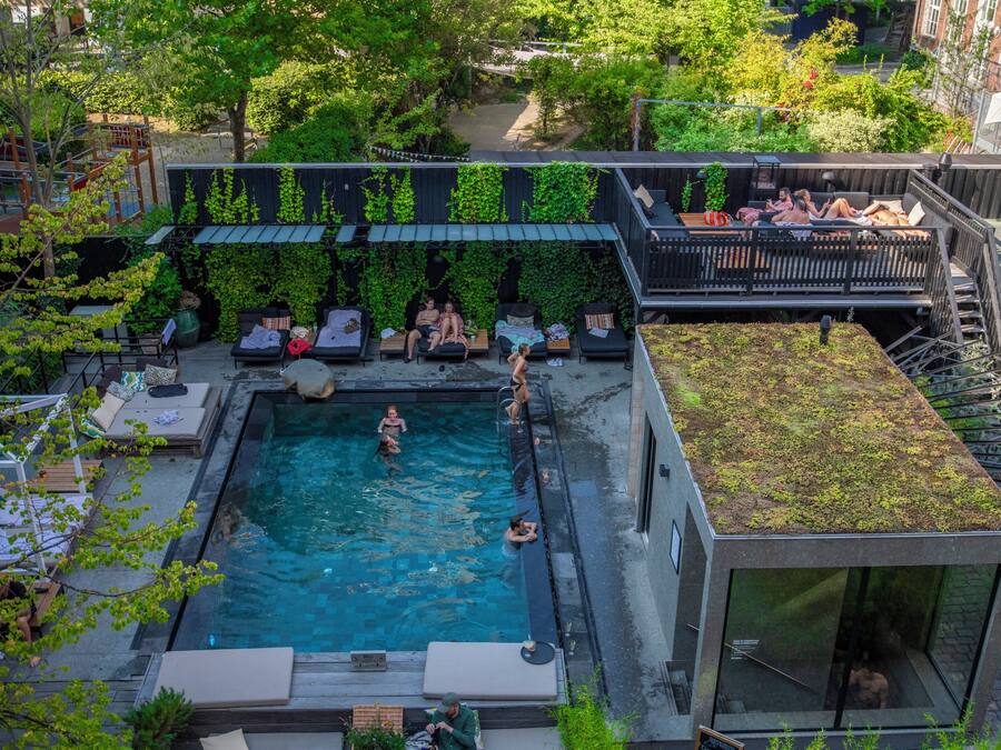 A rooftop pool area with a glass enclosure, lounge seating, and a covered deck with greenery.