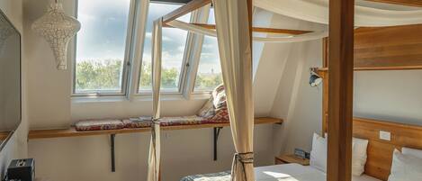A bedroom with a four-poster bed, a desk with a telephone, and a window with a view of trees.