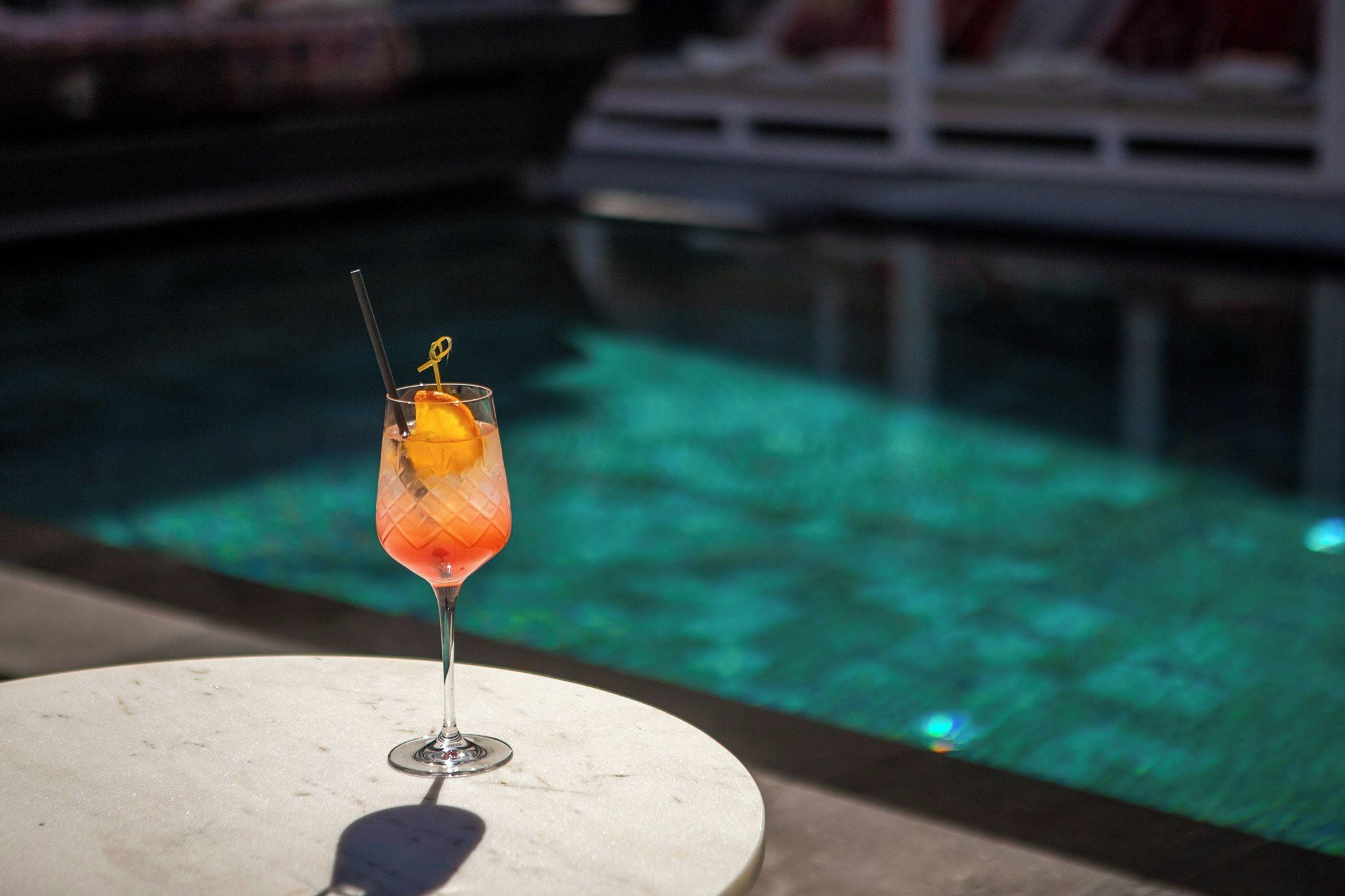 Ein Cocktailglas mit Trinkhalm und Garnitur auf einem runden Tisch am Pool.