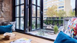 Une pièce dotée d’une grande fenêtre, d’une table en bois et offrant une vue sur un bâtiment et un jardin.