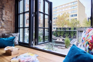 Una habitación con un ventanal grande, una mesa de madera y vistas a un edificio y un jardín.