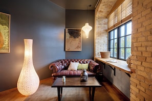 A cozy room with a leather sofa, a table with a vase and a candle, a hanging light fixture, and a window with a view of trees. - Bryggen Guldsmeden (Copenhagen)