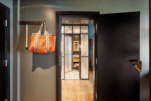 Un pasillo con piso de madera, una puerta oscura con un ojo de cerradura y un bolso colgado de un gancho.