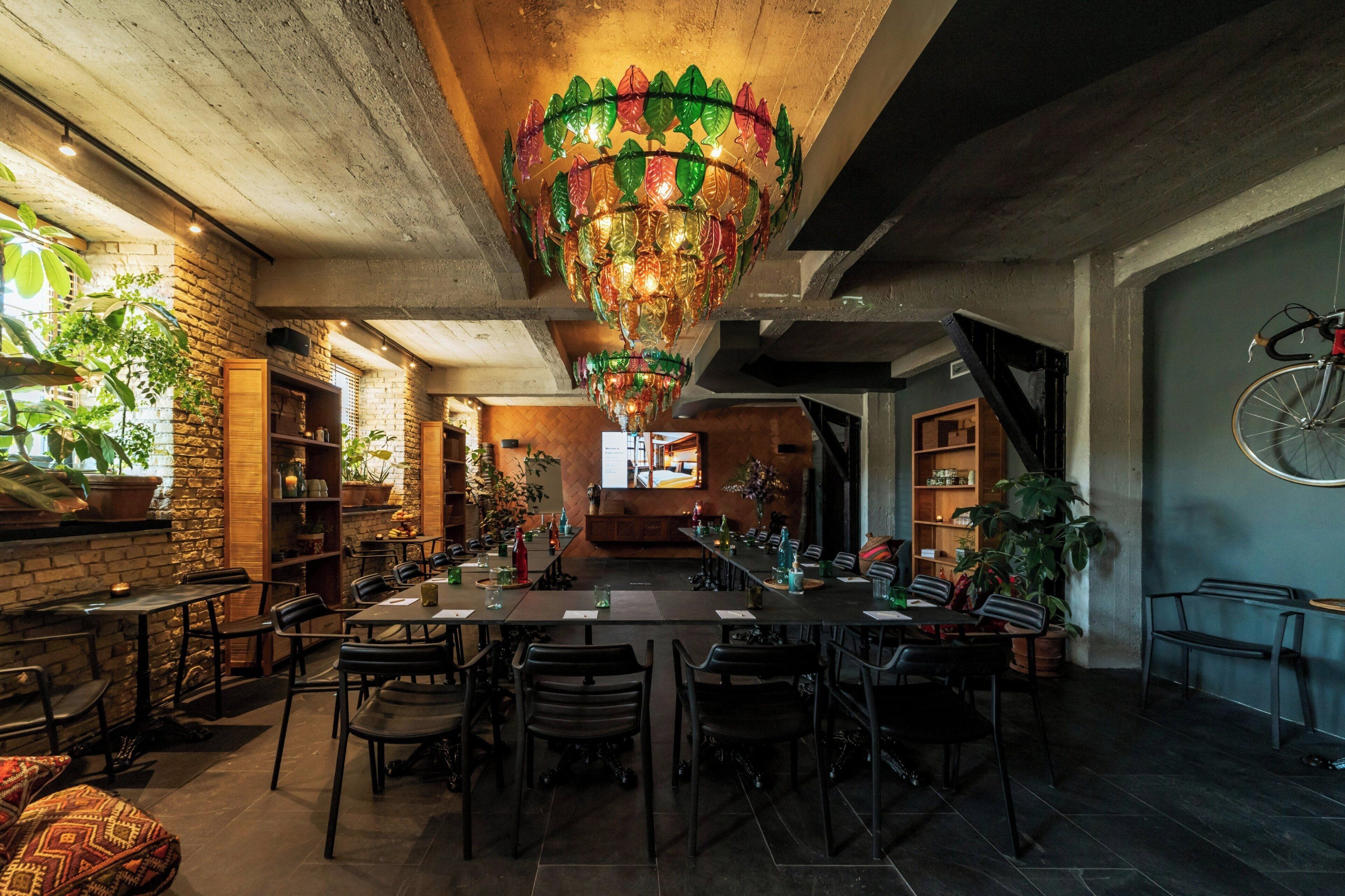 A restaurant with a long communal table, chairs, and a hanging decorative light fixture.
