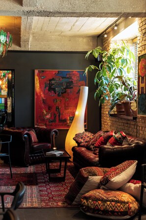 Een gezellige woonkamer met leren banken, een groot abstract schilderij, een hoge vloerlamp en een potplant.