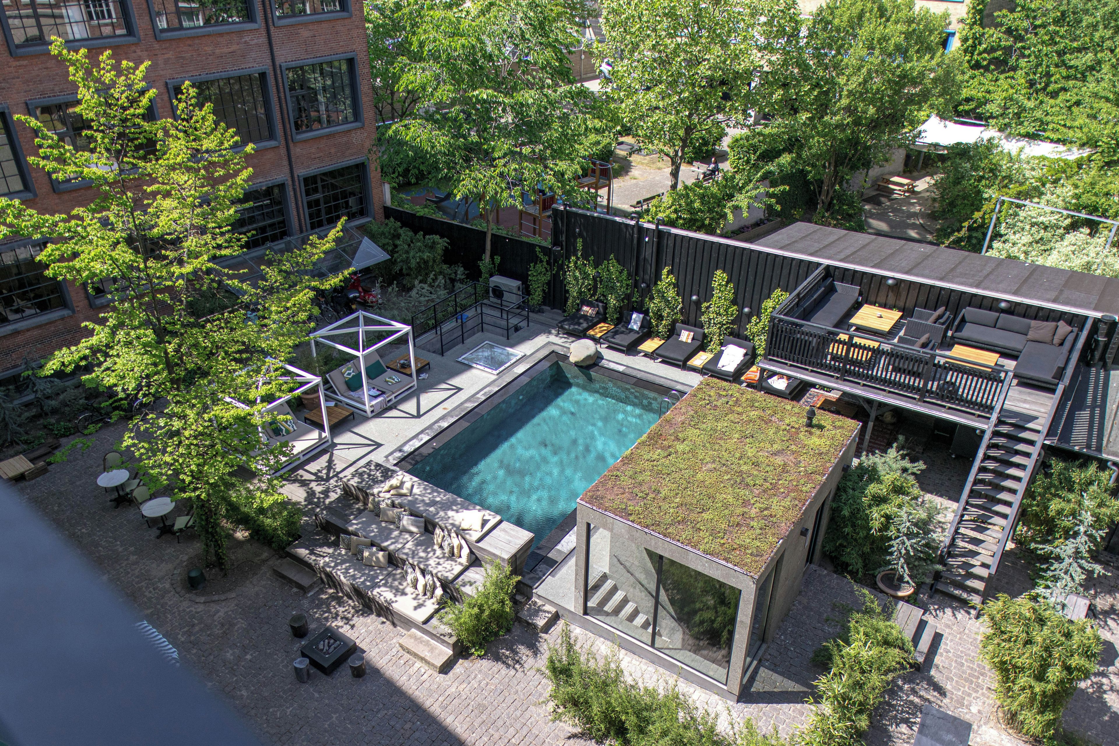 An aerial view of a rooftop pool area with multiple seating areas, a small pool, and surrounding greenery.