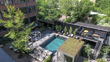 An aerial view of a rooftop pool area with multiple seating areas, a small pool, and surrounding greenery.