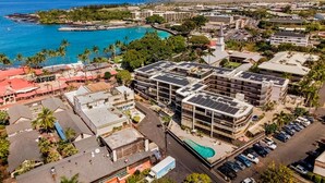 Vista aérea de una zona urbana costera con un edificio de varios pisos destacado, que cuenta con paneles solares, piscina y estacionamiento.