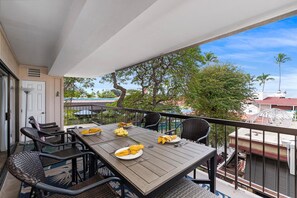 A balcony with a table set for two, chairs, and a view of trees and buildings.