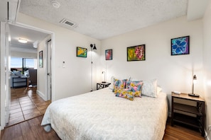 Quarto com uma cama, mesa de cabeceira, abajur e obra de arte na parede.