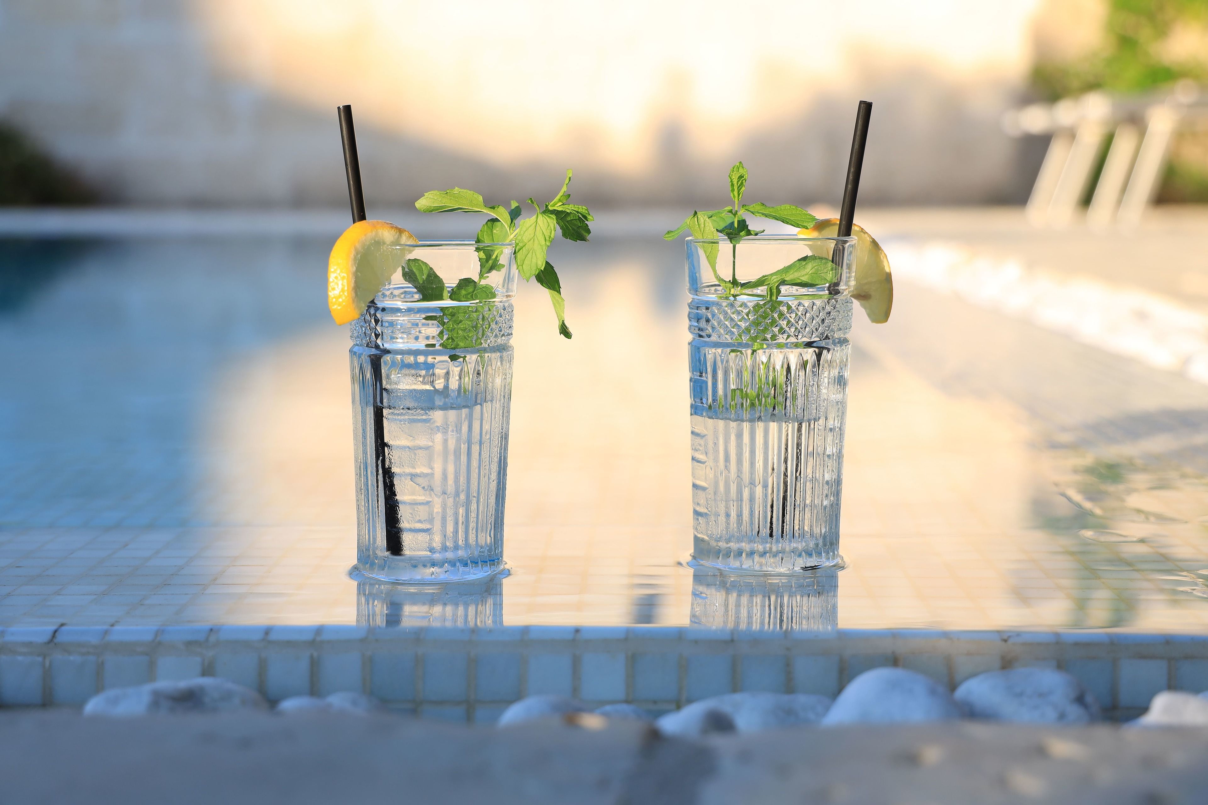 Two glasses of water with mint leaves and lemon slices on a tiled poolside.