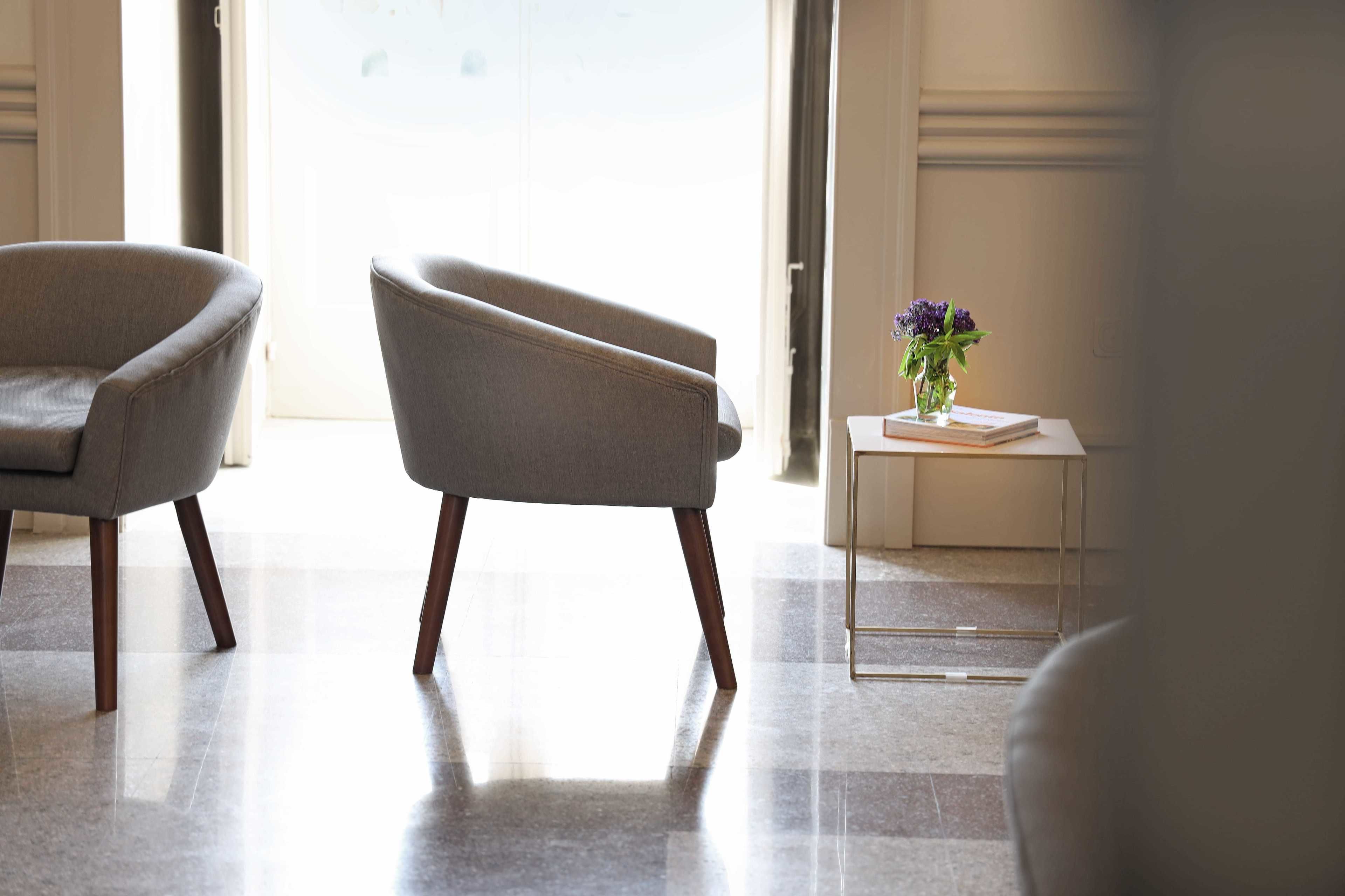 A modern room with two armchairs, a small side table with a vase of flowers, and a door leading to a bright area.