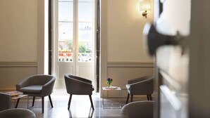Un hall de hotel con vistas a través de un ventanal, que cuenta con una zona de estar con sillones y una pequeña mesa con un jarrón de flores.