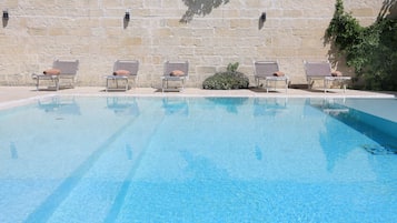 Una piscina al aire libre, sombrillas, sillones reclinables de piscina