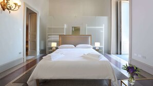 Habitación de hotel con una cama grande, dos mesitas de noche con lámparas, un espejo sobre la cama y vista al pasillo.