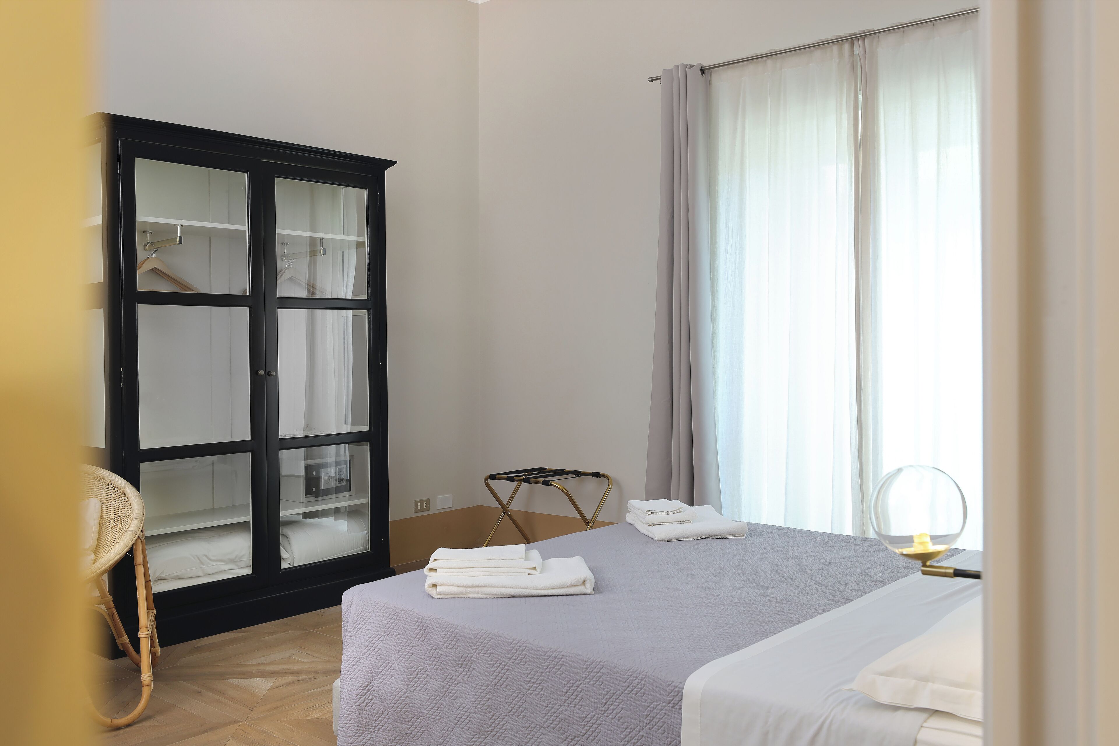 A hotel room with a bed, a wardrobe, a chair, and a window with curtains.