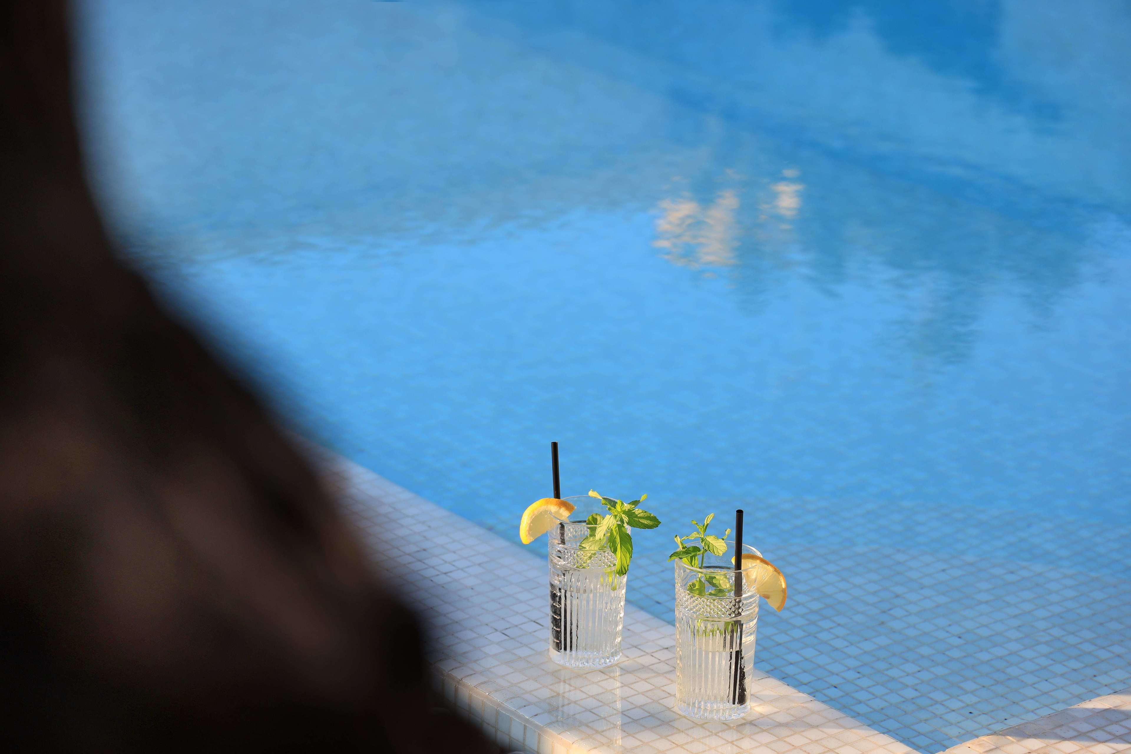 Dos vasos de una bebida con hojas de menta y rodajas de limón en una zona junto a la piscina.