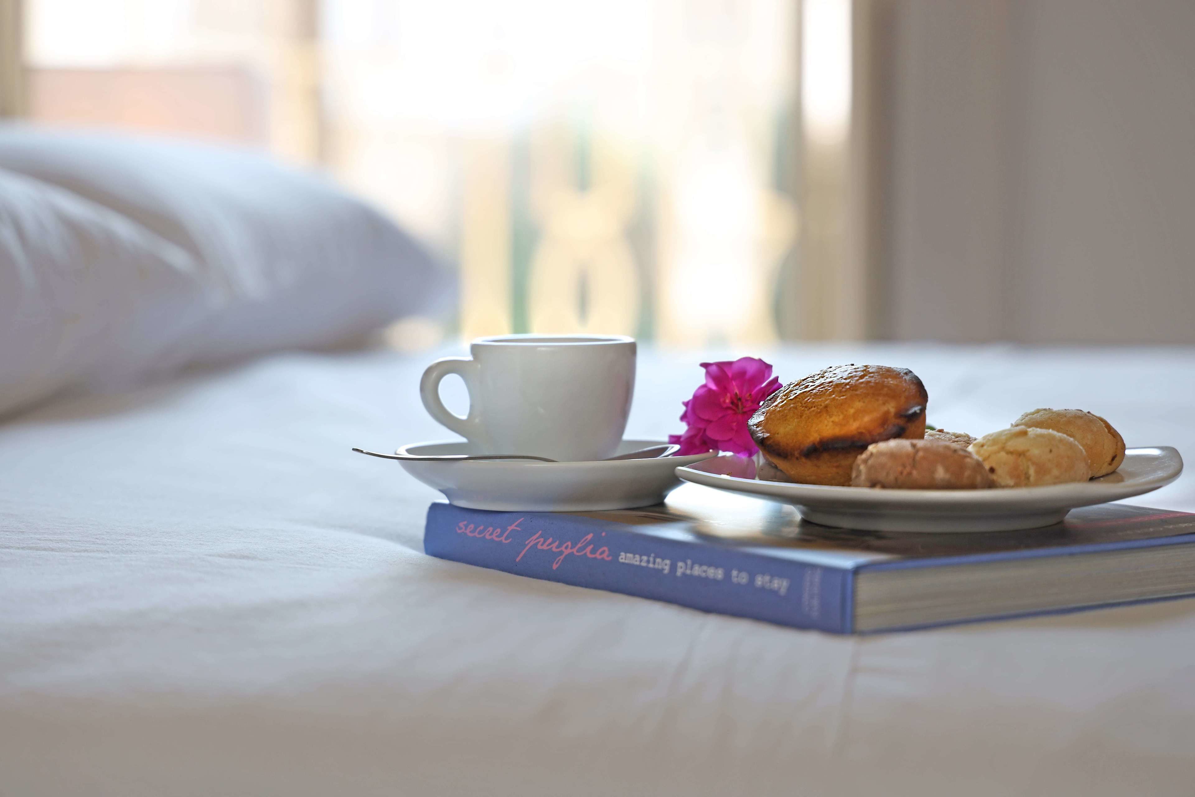 A bed with a white pillow, a cup of coffee, a plate of pastries, and a book titled 'secret puebla amazing places to stay'.