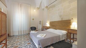 Een hotelkamer met een bed, een stoel, een nachtkastje, een lamp en een spiegel.