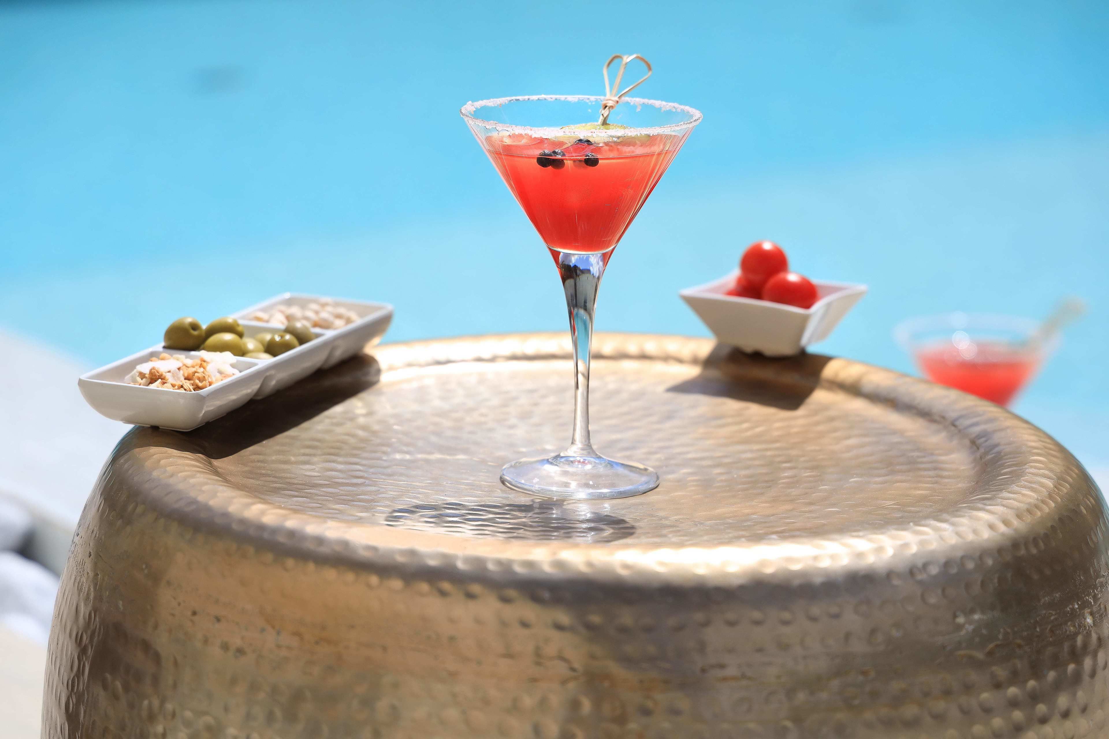 A martini glass with a cherry garnish on a textured metal table.