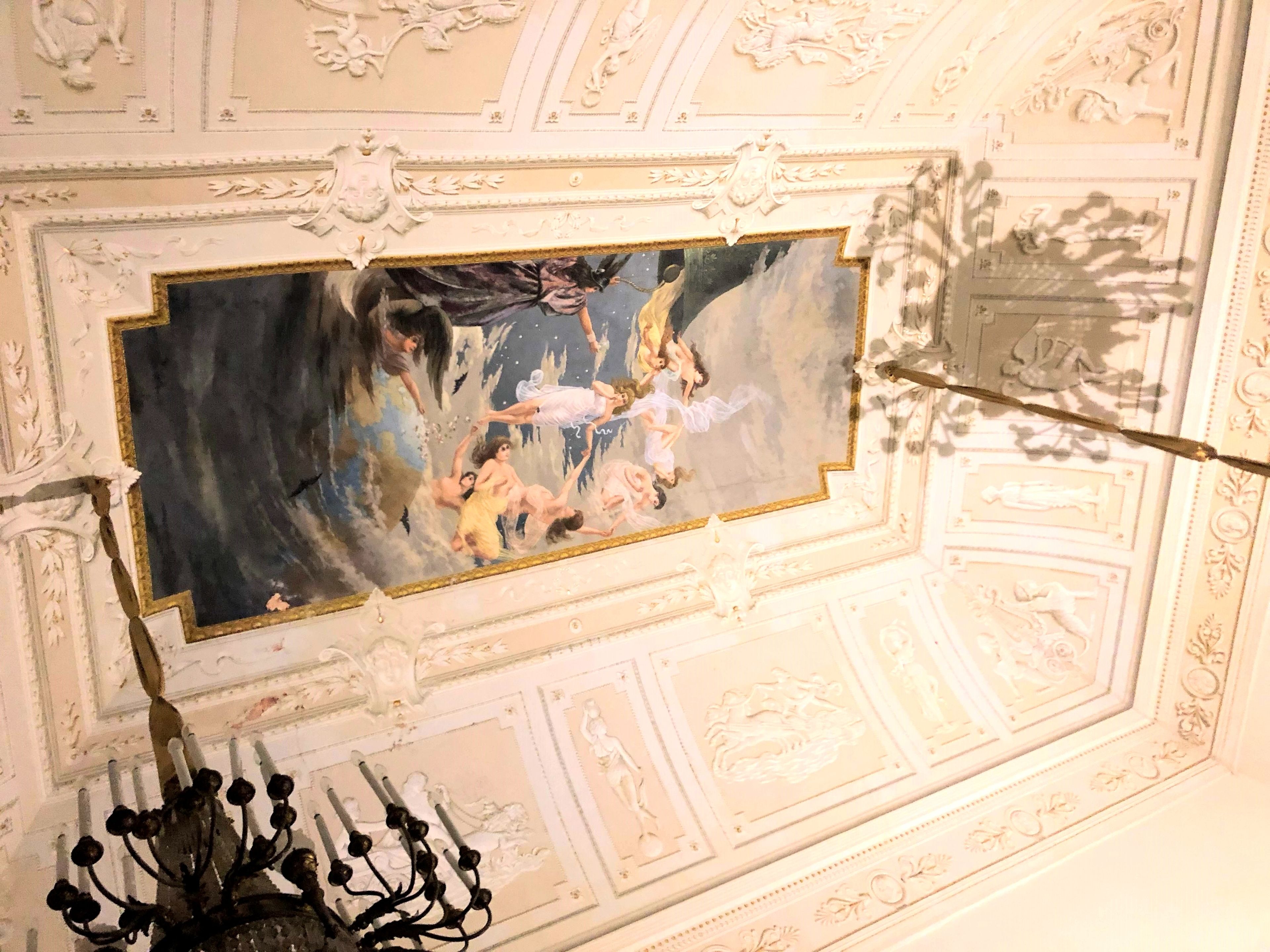 Techo con delicados trabajos de yeso blanco y una pintura central que representa una escena mitológica.