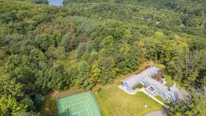 Vista aèria d'una casa envoltada de bosc dens, amb una pista de tennis visible a l'esquerra.