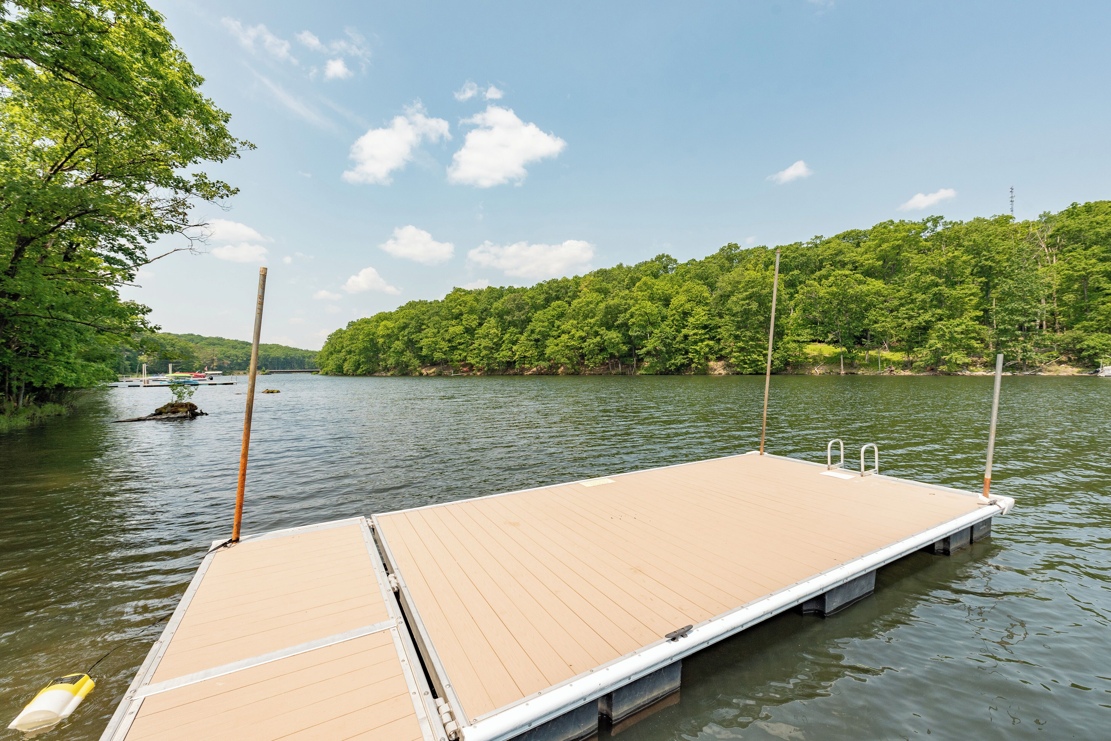 A wooden dock extending into a calm lake, surrounded by lush greenery and a clear sky.
