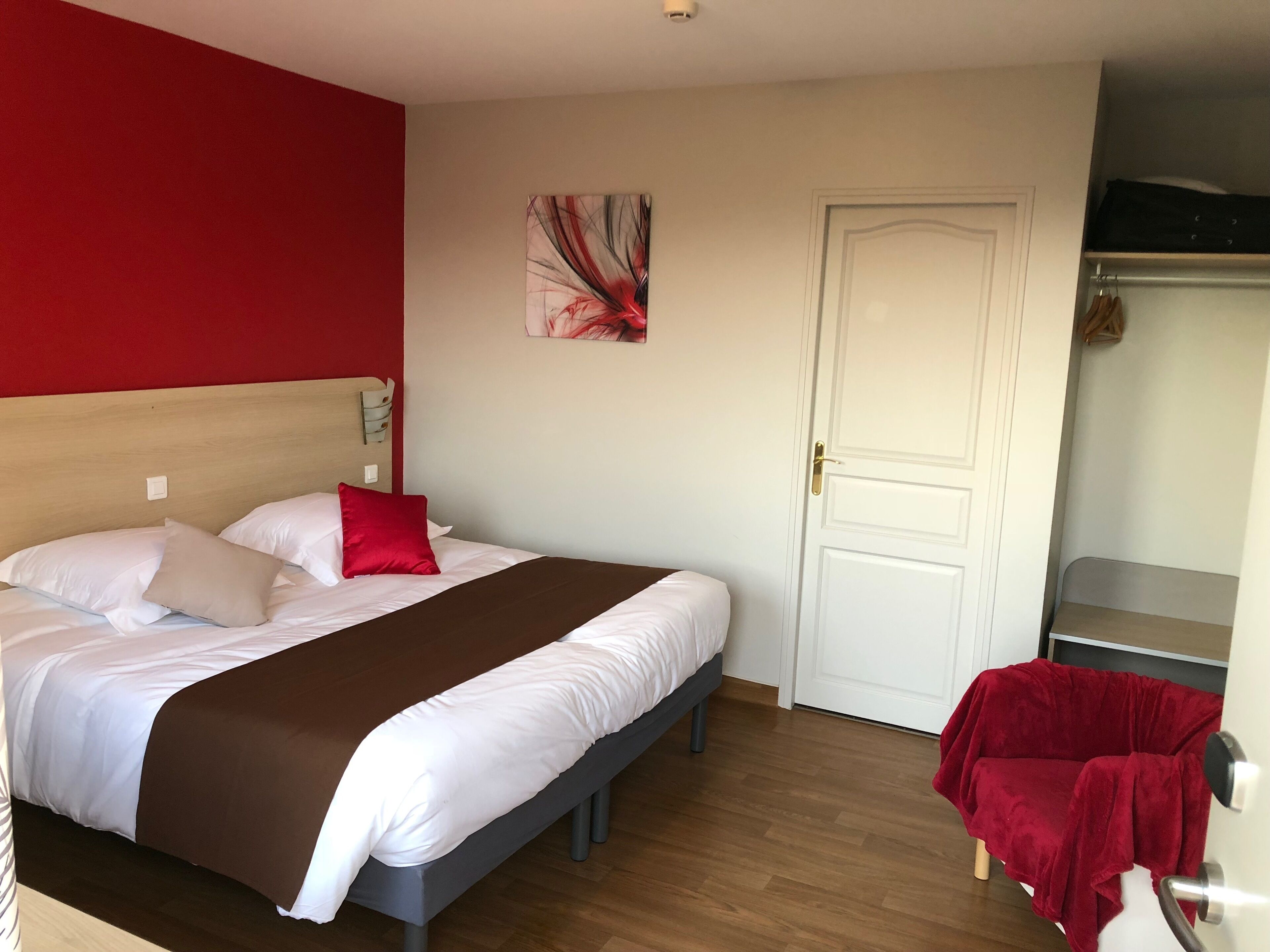 A neatly made bed with white and brown bedding, a red pillow, and a wooden headboard.