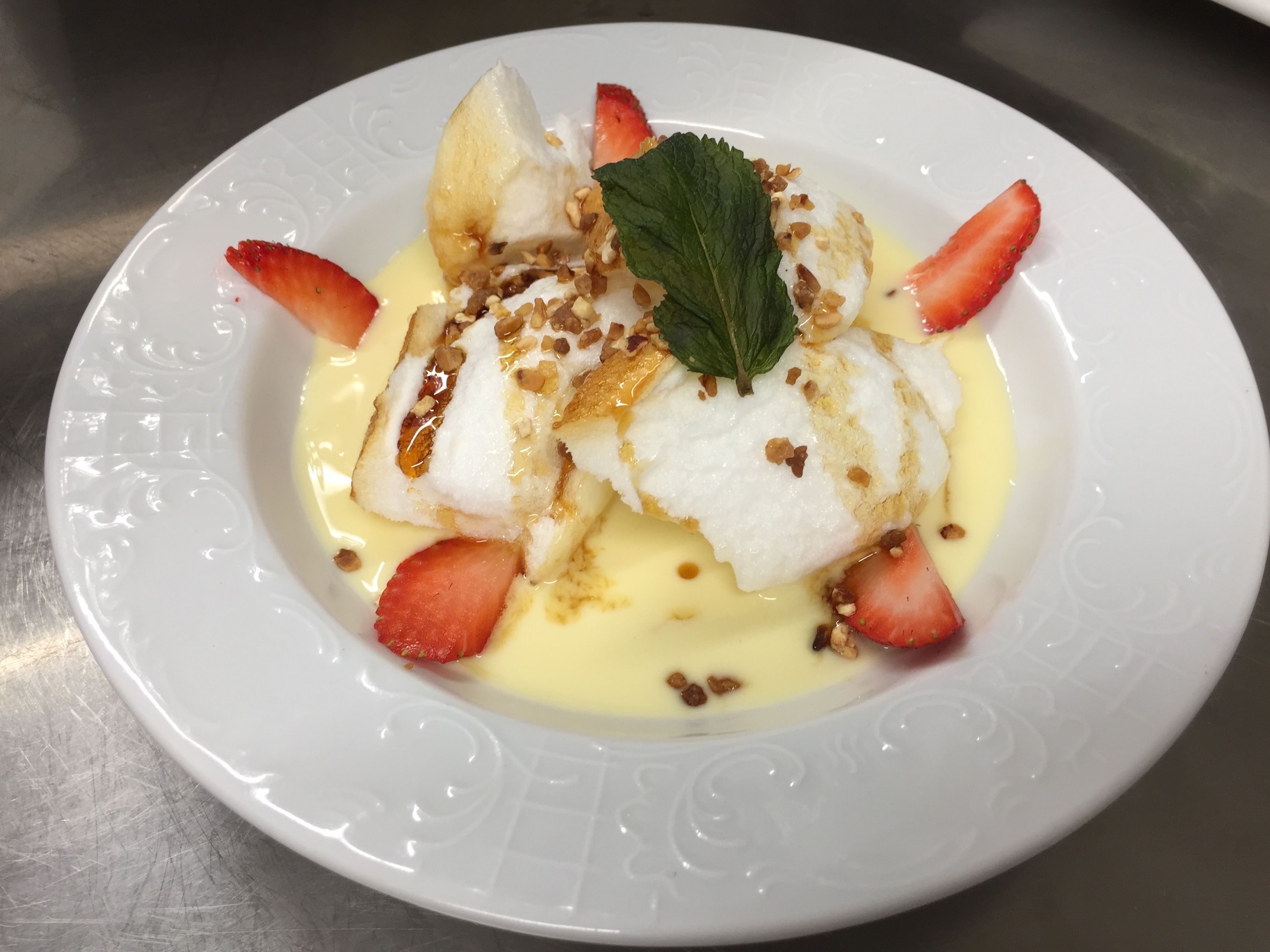 A white plate with a dessert consisting of white cake, strawberries, and a yellow sauce.